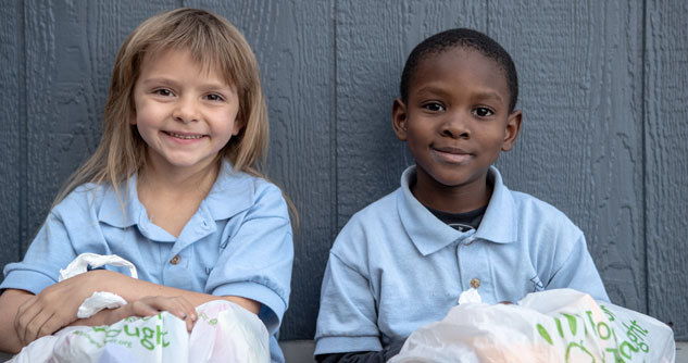 Two smiling children wearing light blue polos with sacks of food