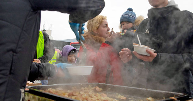 Ukrainian refugee mom feeds baby some sausage.