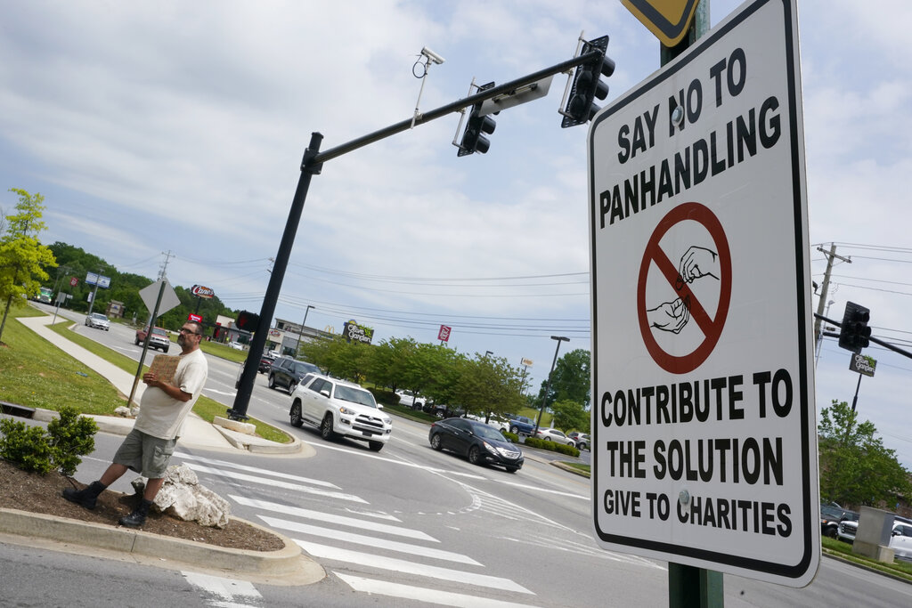 Adam Atnip, who is homeless and lives in his car, panhandles near a sign asking people not to give directly to panhandlers