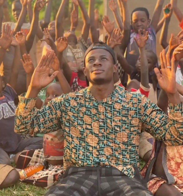 Man with hands raised with dozens of children behind him, worshipping God.