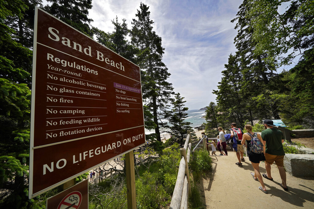 Beach-goers walk by a sign that warns of the absence of lifeguards at Sand Beach in Acadia National Park near Bar Harbor, Maine