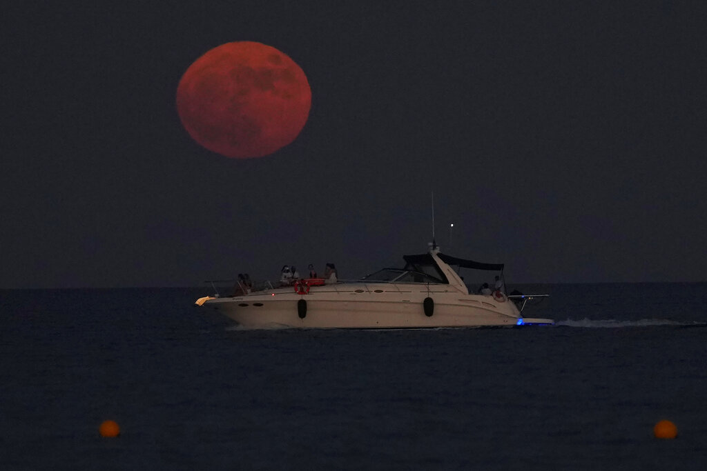 The full moon rises over the Mediterranean sea as people on a boat enjoy, in southern coastal city of Larnaca, in the southeast island of Cyprus, on Wednesday, July 13, 2022.
