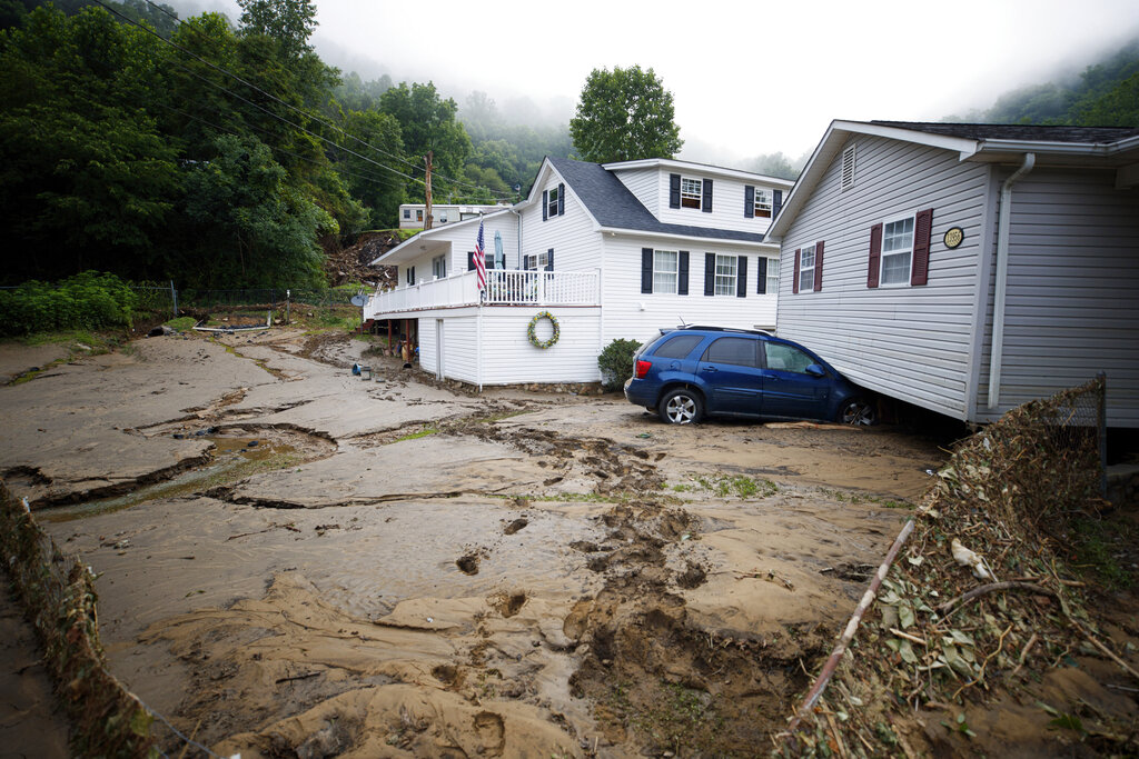 A house that was moved off of its foundation following a flash flood rests on top of a vehicle