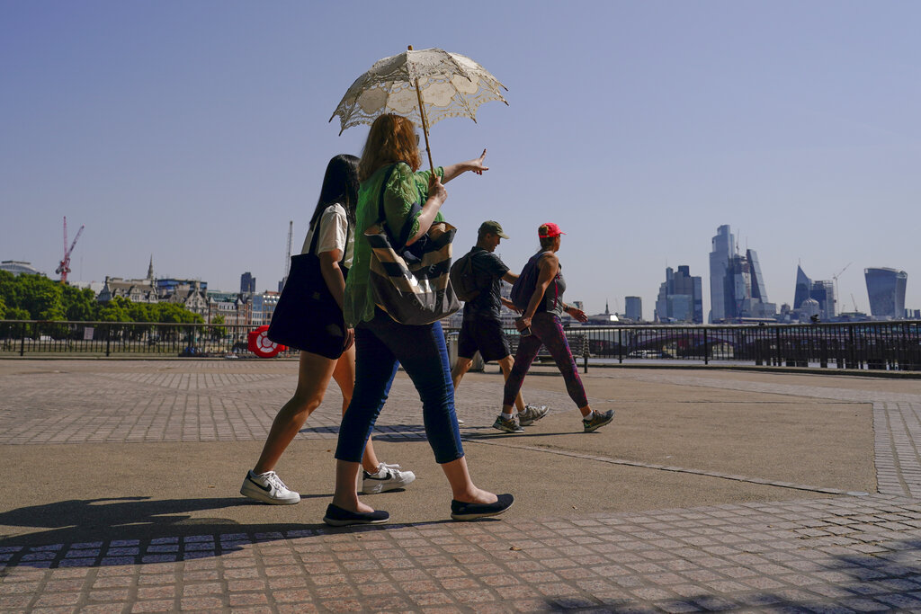 A woman holds an umbrella to shelter from the sun, as she walks on the south bank of river Thames, in London