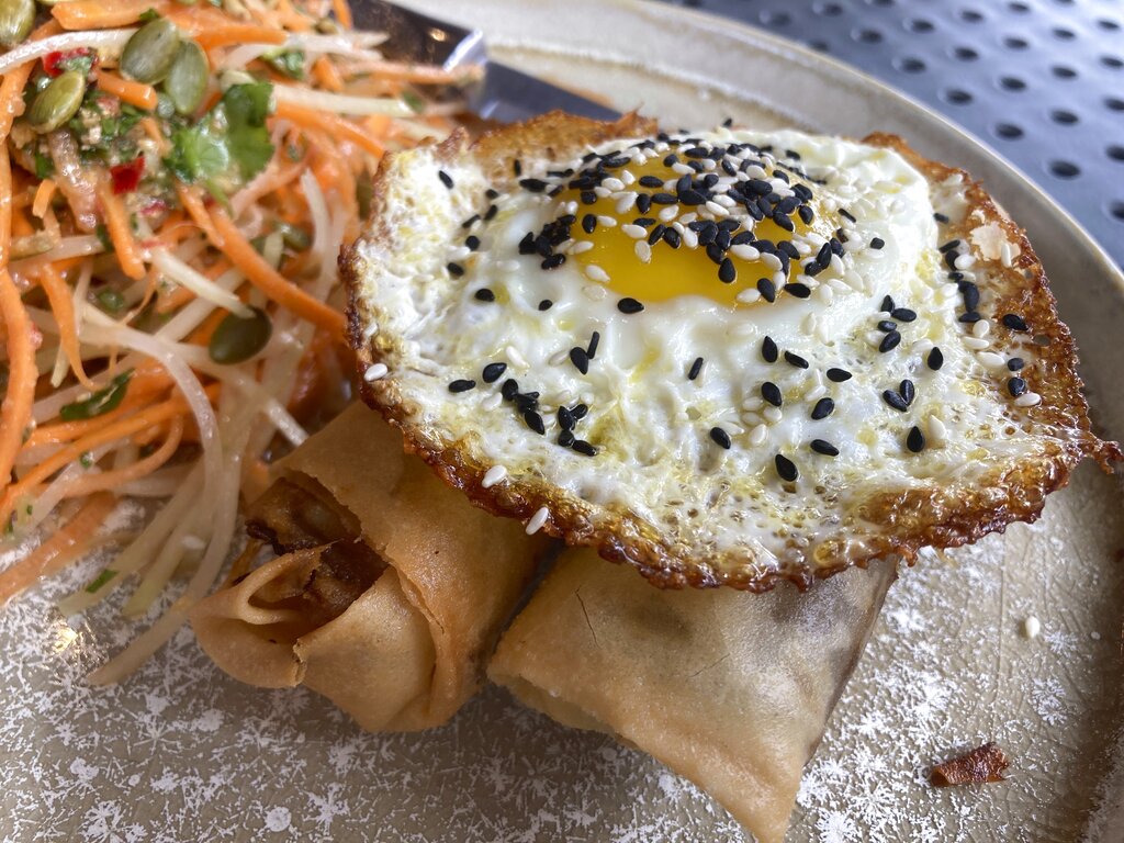 A vegan chorizo egg roll and a meat chorizo egg roll topped with a fried egg and a papaya and carrot slaw 