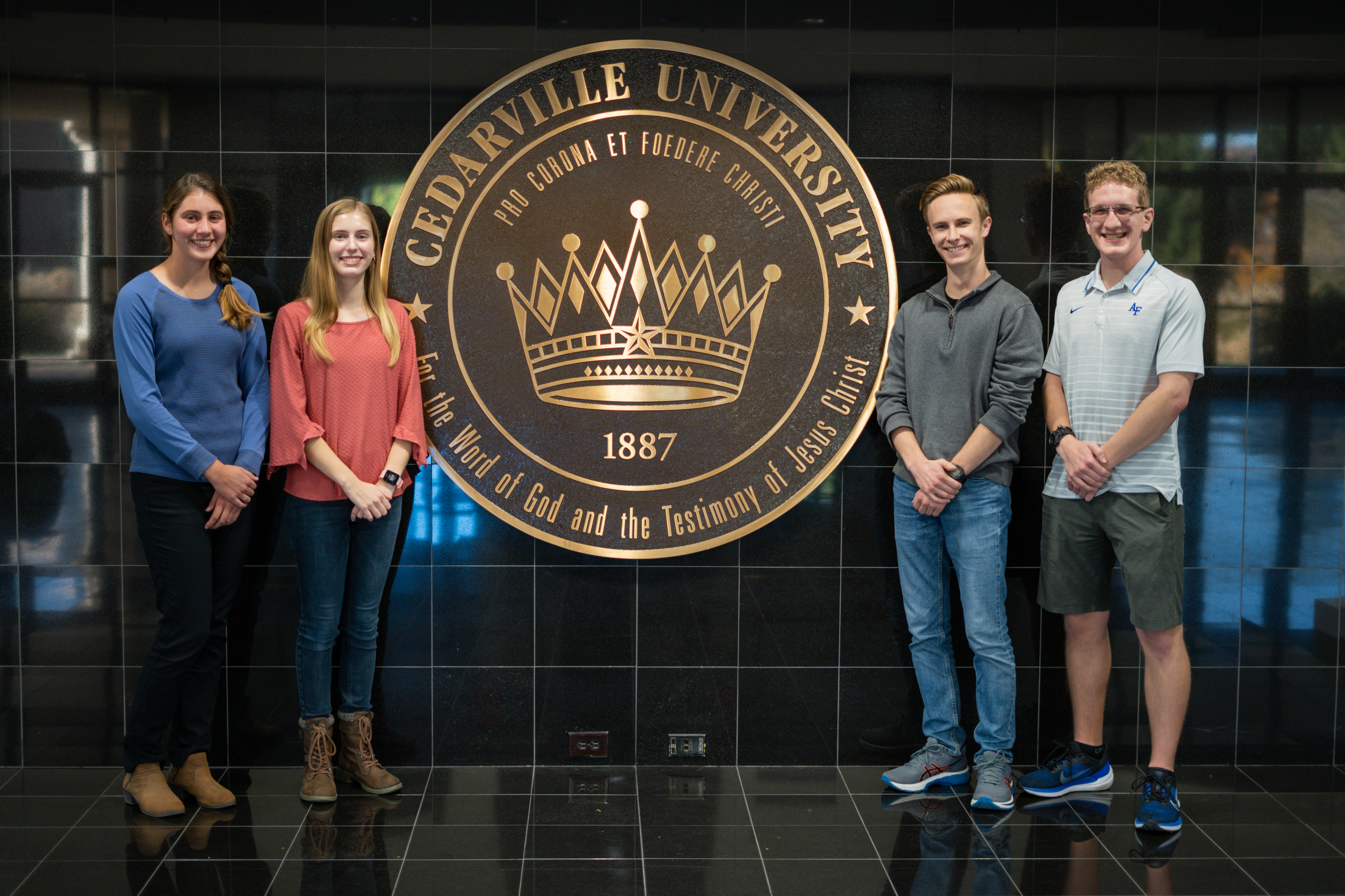 Anna, Sarah-Kate, Simon and Kai stand in front of the Dixon Ministry Center seal