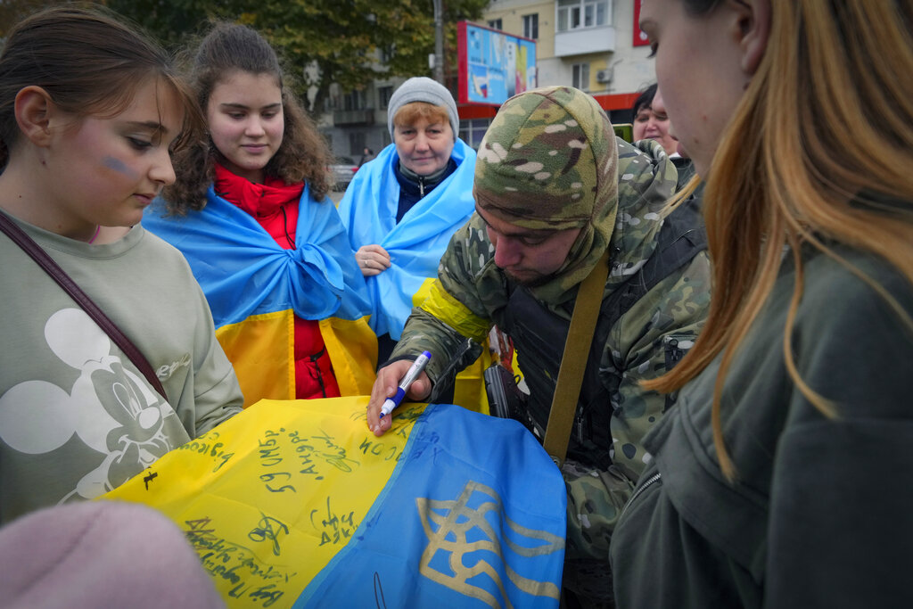 A Ukrainian soldier writes: "From the Ukrainian Armed Forces" on the national flag for a local resident in central Kherson