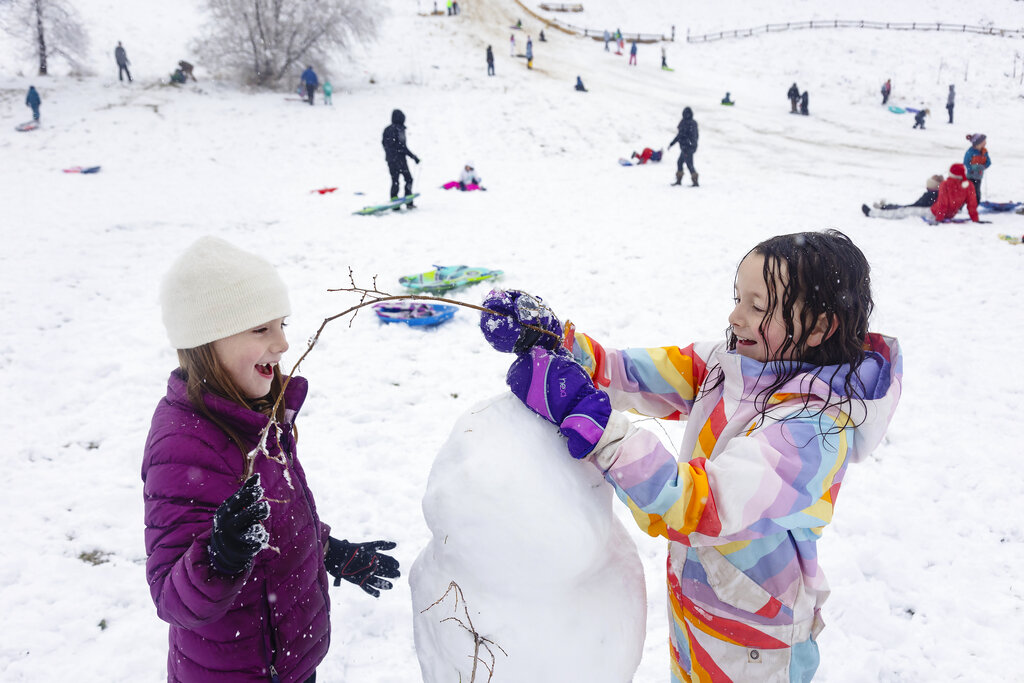 Girls use tree branches to make arms and even hair on their snowman in Boise, Idaho