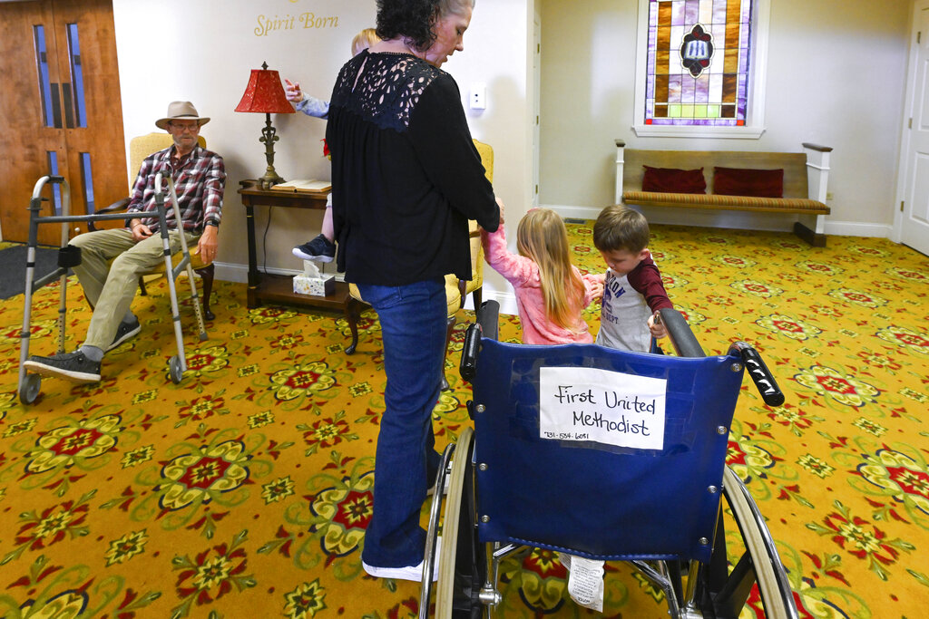 Jerry Lamb, who has a spine condition, sits in a chair in the lobby as his wife, Laura, tends to their foster kids, Adriana McCartney, and Charlie Mitchell at Camden First United Methodist Church