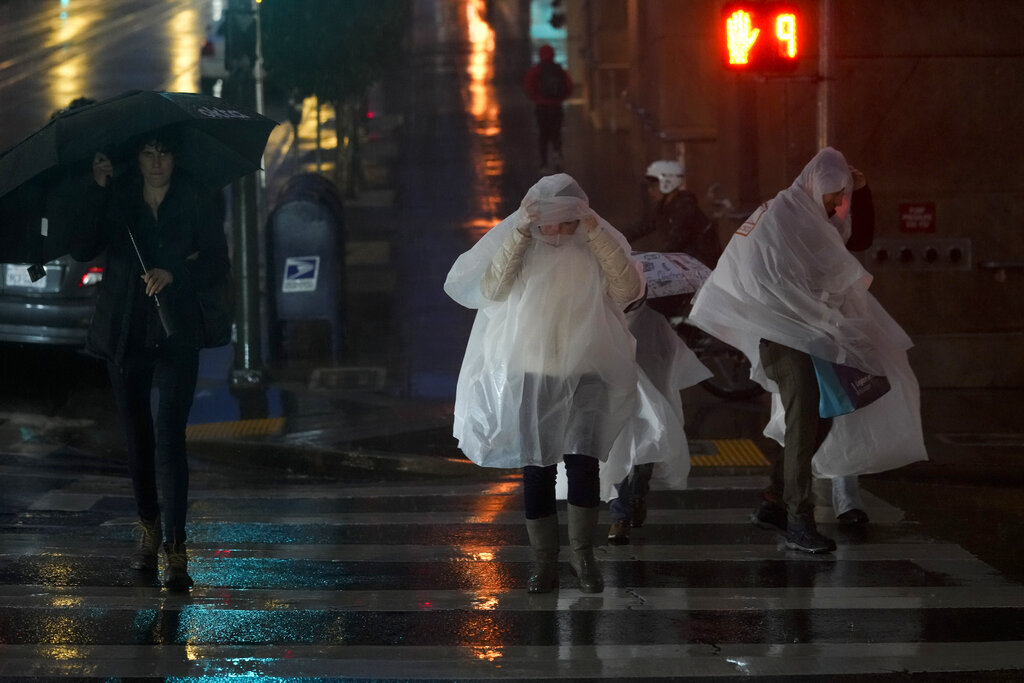 People wearing rain ponchos walk across Kearny Street in San Francisco