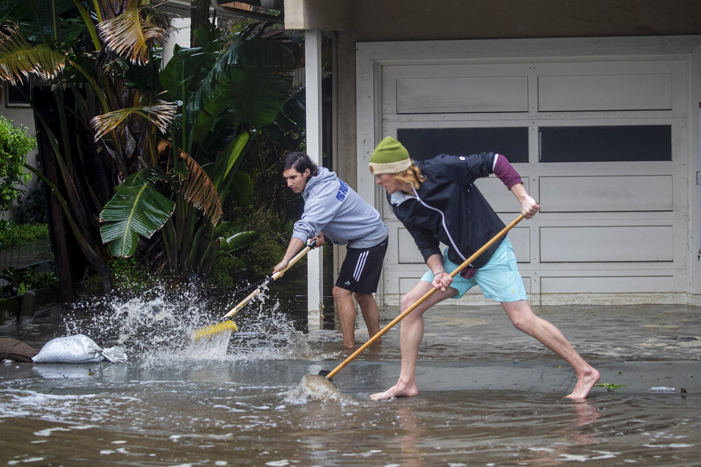 Evan Sousa, left, gets help from Calvin Drake pushing water out of his flooded apartment on Palmetto Avenue in Pacifica, Calif.