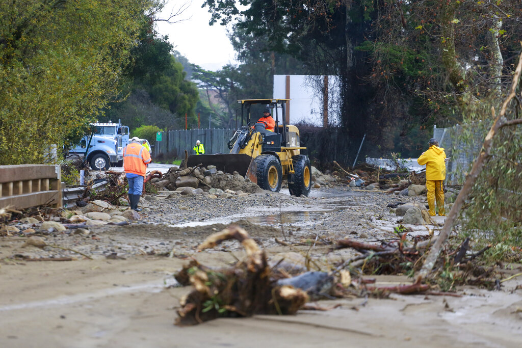 A work crew cleans up an area of Highway 101 that flooded in Montecito, Calif.