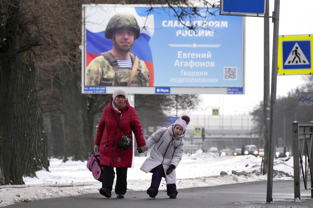 A woman and a girl walk past a billboard with a portrait of a Russian officer awarded for action in Ukraine and the words "Glory to the heroes of Russia" in St. Petersburg, Russia