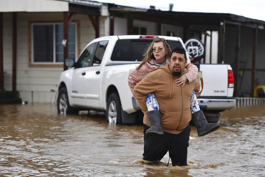 Ryan Orosco, of Brentwood, carries his wife Amanda Orosco, from their flooded home on Bixler Road in Brentwood, Calif.