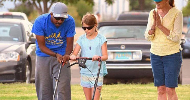 Rodney Smith Jr., bent over helping young girl mow a lawn
