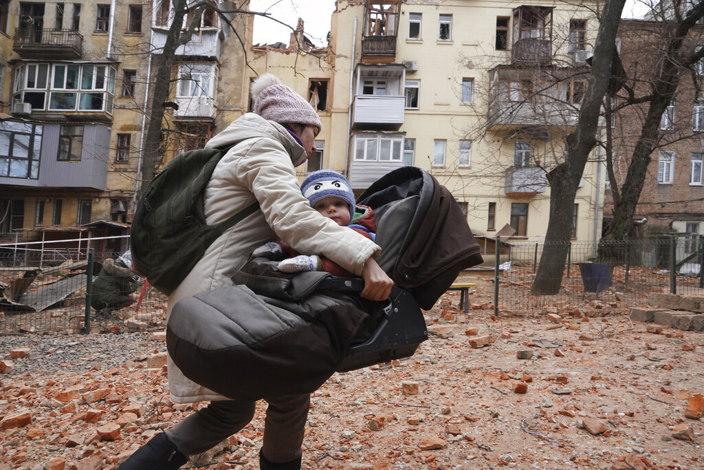A woman carries her child as they evacuate from a residential building which was hit by a Russian rocket at the city center of Kharkiv, Ukraine