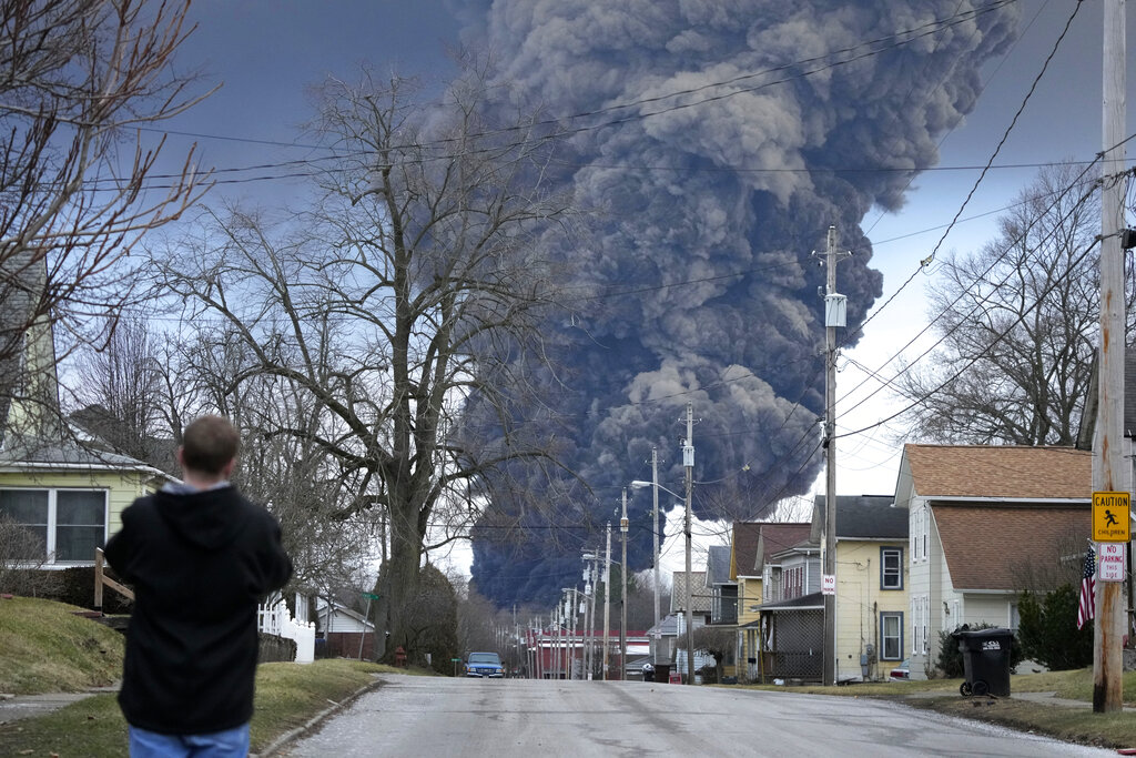 A man takes photos as a black plume rises over East Palestine, Ohio