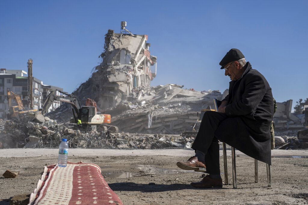 Mehmet Nasir Duran, 67, sits on a chair, as heavy machines remove debris from a building, where five of his family members are trapped in Nurdagi, southeastern Turkey