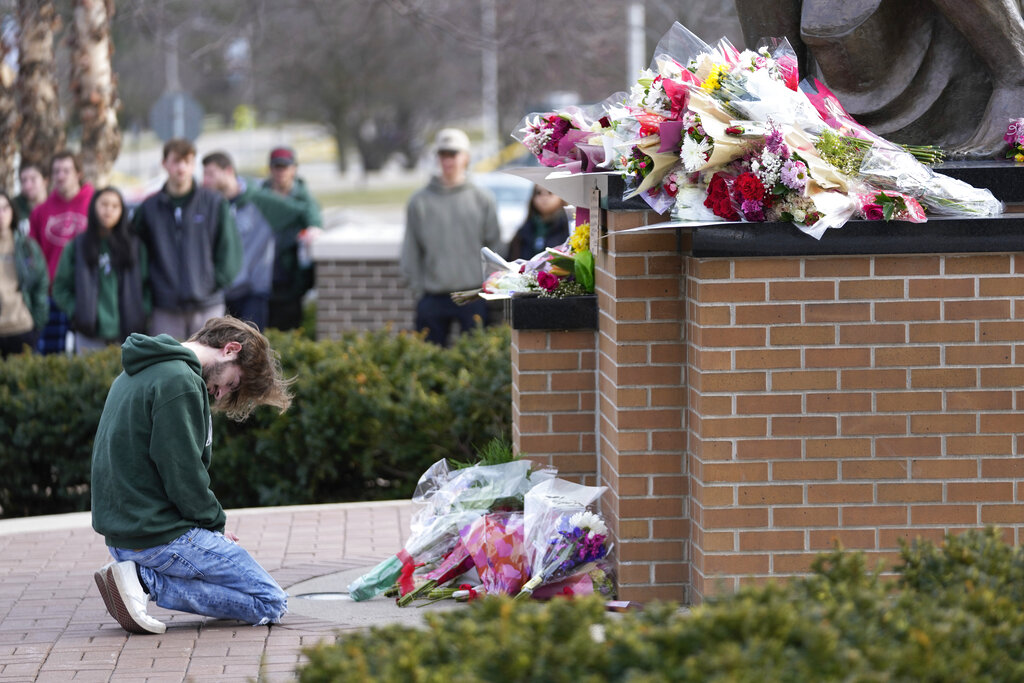 A student kneels where flowers are being left at the Spartan Statue on the grounds of Michigan State University, in East Lansing, Mich.