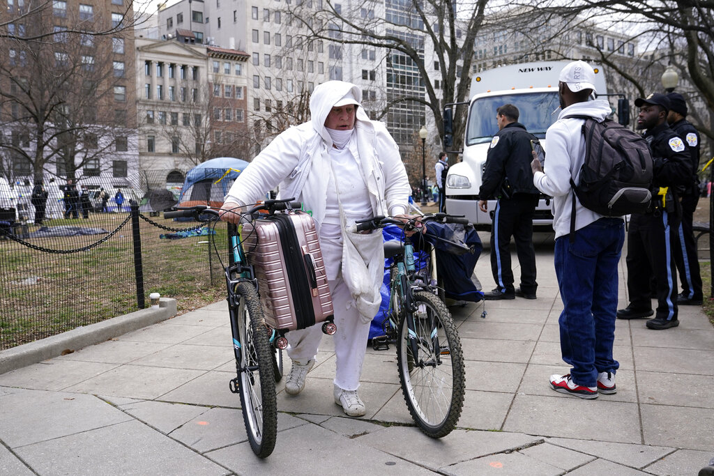 A woman carries belongings out of a homeless encampment at McPherson Square