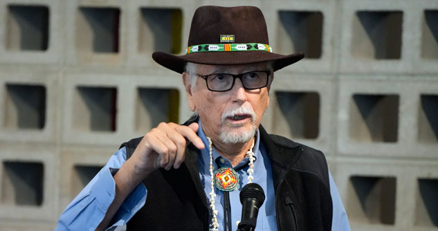 Man in brown hat with Native American beaded jewelry on hat and around his neck