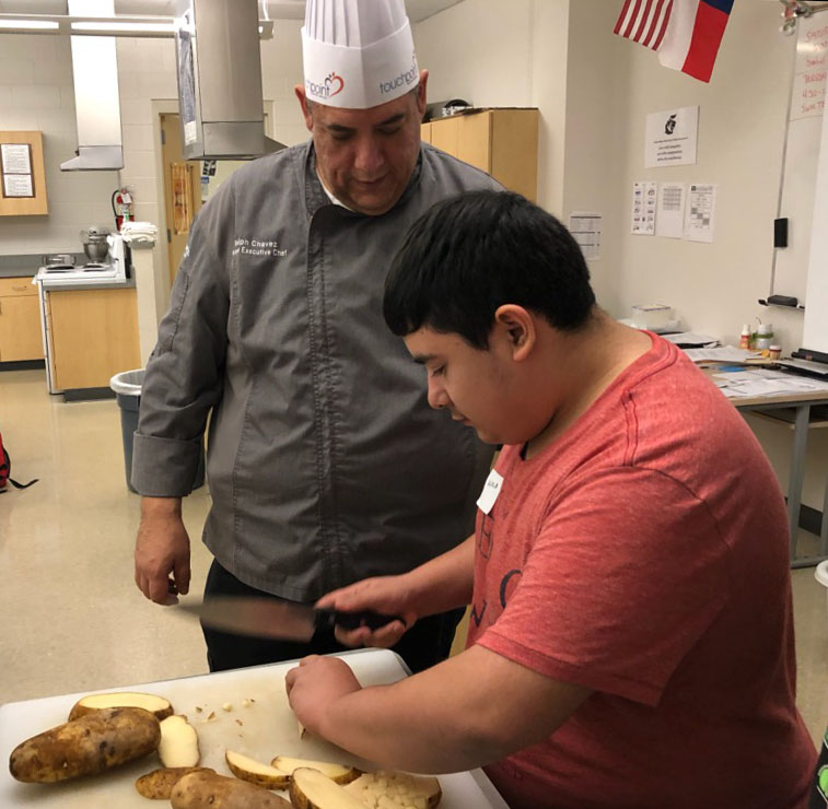 Student Caiden Gonzales practices proper cutting technique with Chef Ralph Chavez 
