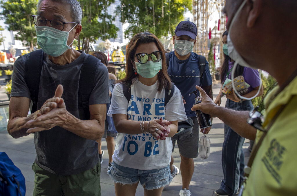 A doorman distributes hand sanitizing liquid for visitors at a luxury mall in Bangkok, Thailand